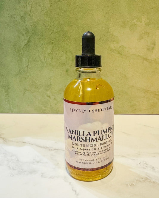 A bottle of Lovely Essentials Vanilla Pumpkin Marshmallow moisturizing body oil with a black dropper cap, set on a white marble surface against a textured olive green background.